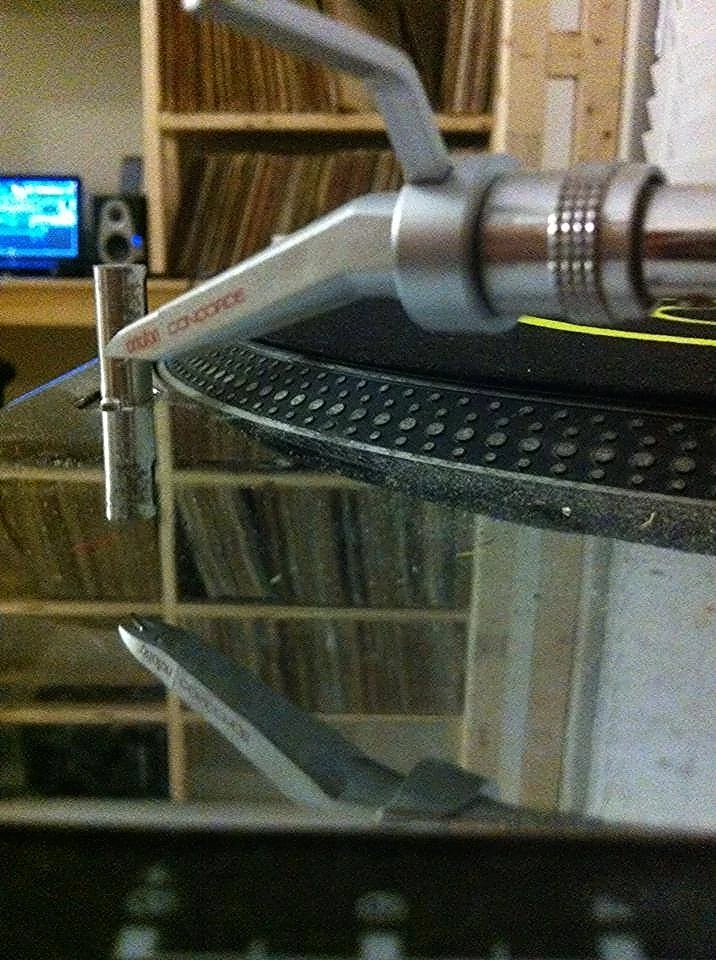Turntable tonearm in front of shelves of vinyl records
