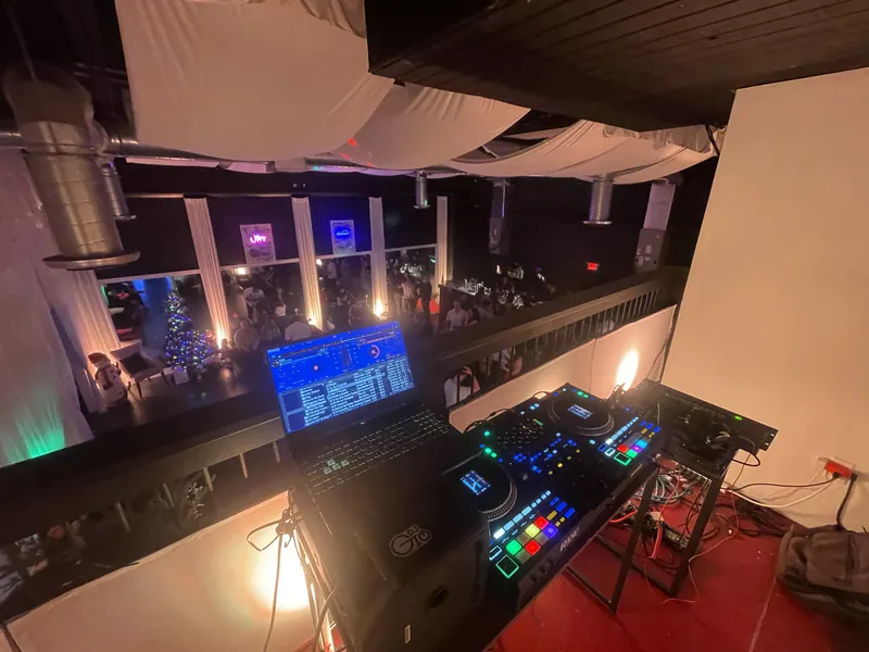 DJ booth on a nightclub balcony overlooking a crowded holiday party
